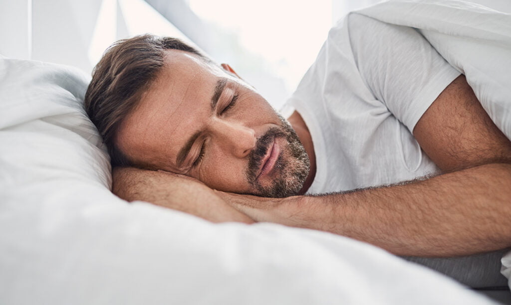 rugklachten na het slapen, man ligt op zijn zij op wit dekbed en kussen