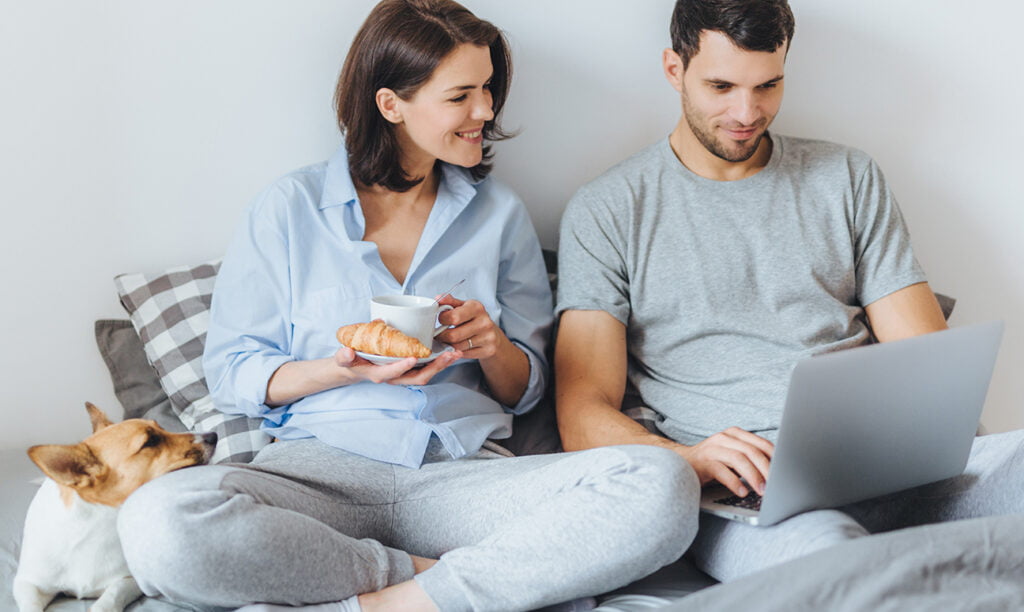 dikte matras bepalen online, vrouw en man zitten op bed achter laptop